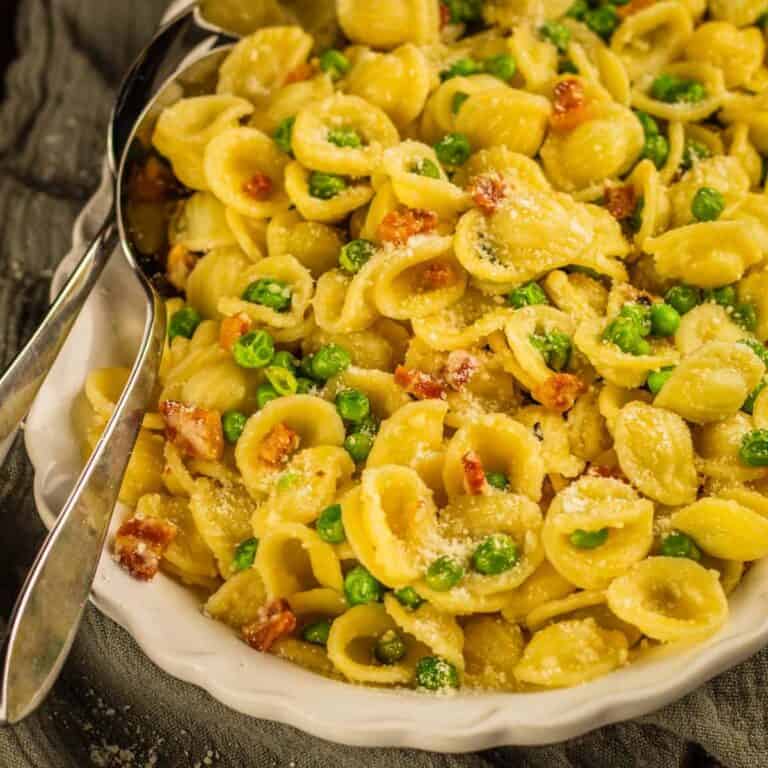 white platter of orecchiette pasta with pancetta pieces and green peas