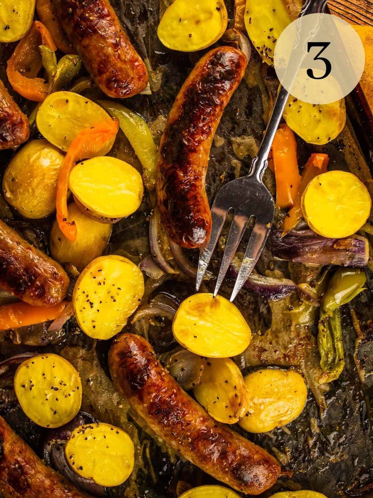 roasted sausages, potatoes, onions and peppers on a sheet pan with serving fork