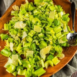raw celery salad with parmesan on a wooden tray with a metal serving spoon