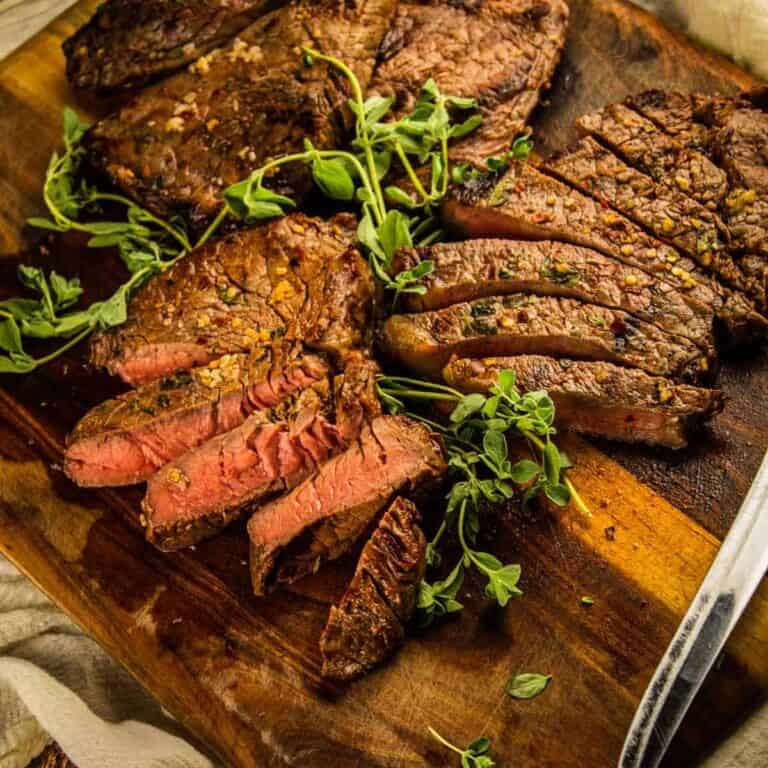 cutting board with partially sliced grilled sirloin steak and fresh oregano stems and knife