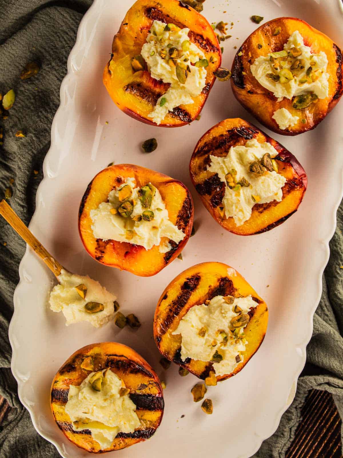 grilled peaches topped with mascarpone and pistachios on a white platter.