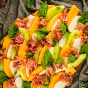 sliced cantaloupe and honeydew with mozzarella, prosciutto and fresh basil on a wooden tray