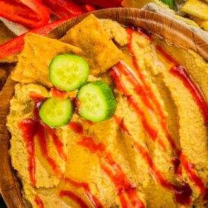 wooden bowl of sriracha flavored hummus with crackers and cucumbers slices in it