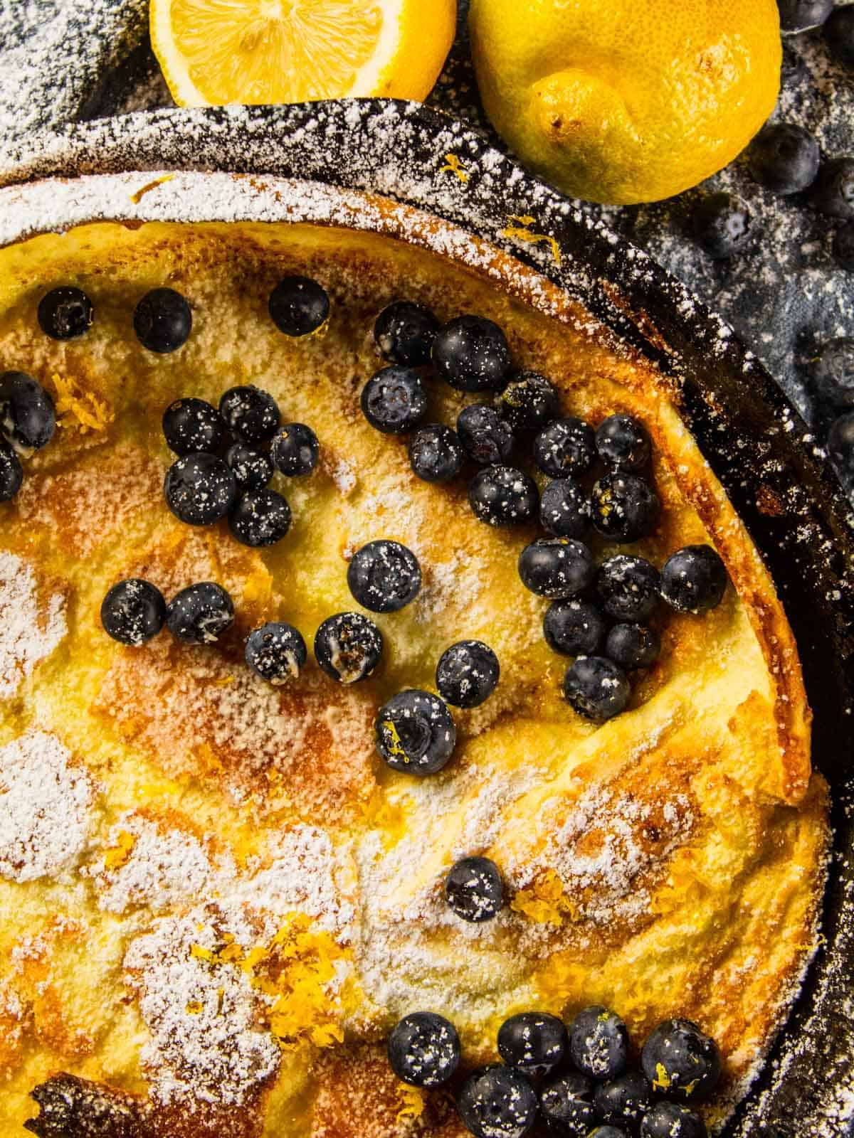 overhead view of a skillet with a dutch baby topped with powdered sugar and fresh blueberries