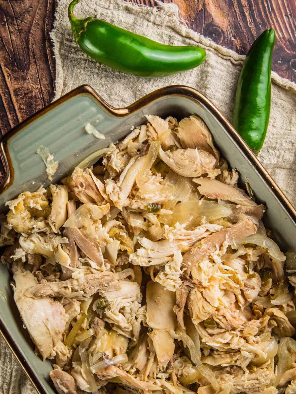 blue ceramic dish filled with shredded chicken and onions with two whole jalapenos next to it 