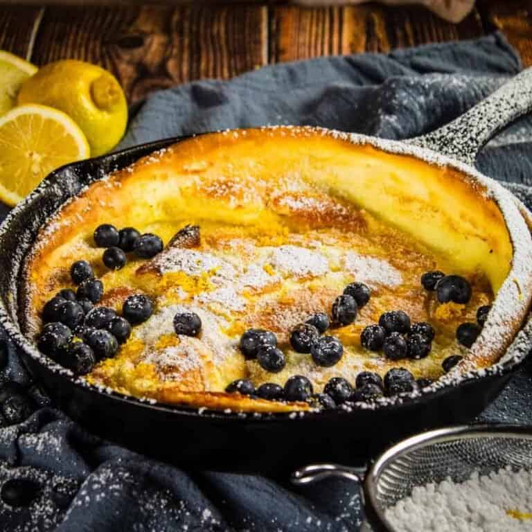 cast iron skillet with german pancake topped with powdered sugar and blueberries