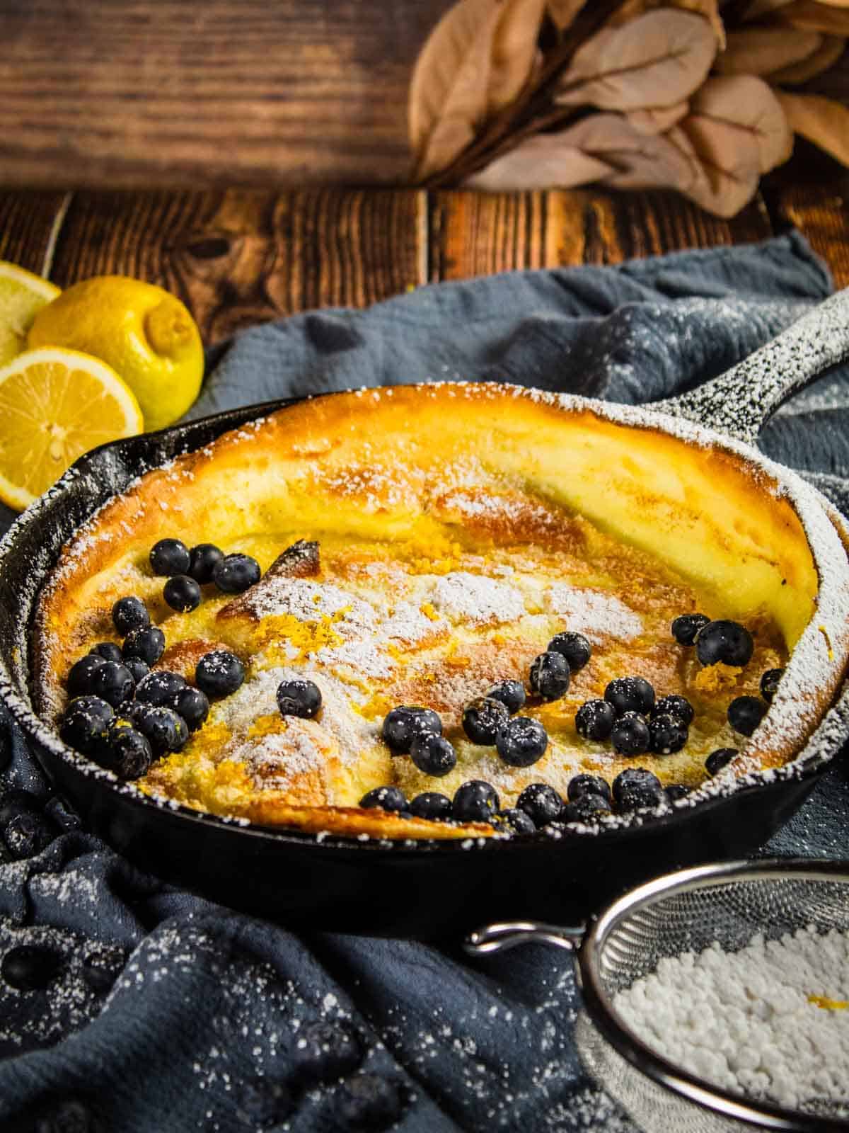 cast iron skillet with a dutch baby topped with powdered sugar and fresh blueberries