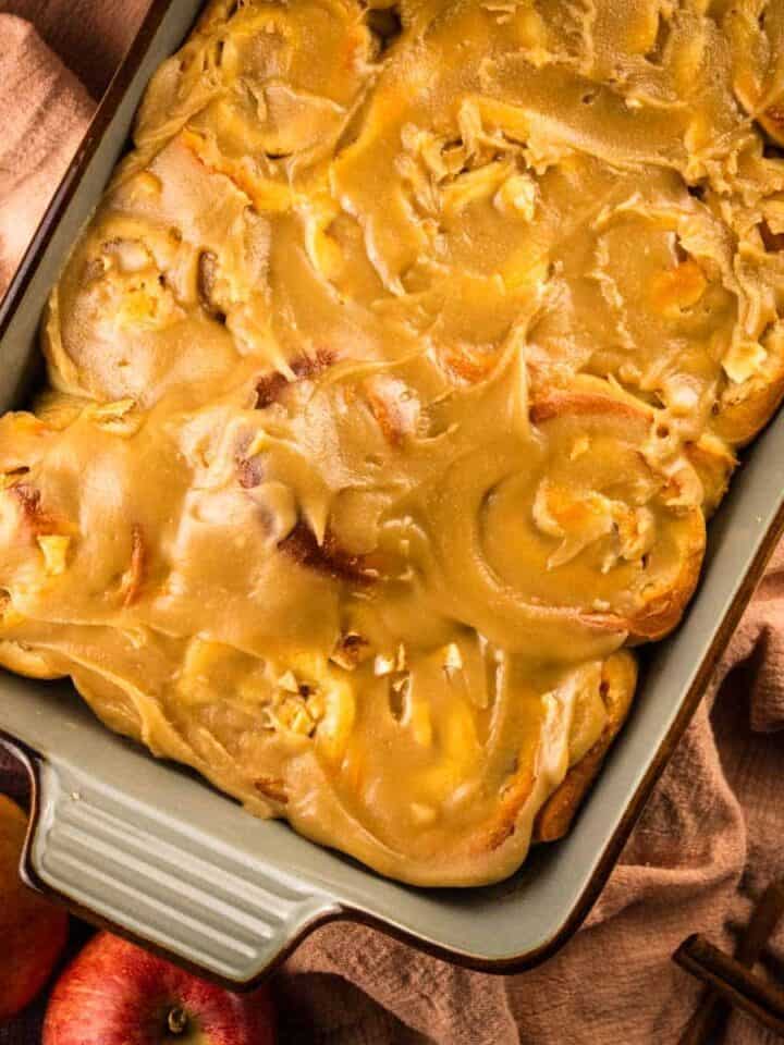 baking dish with apple cinnamon rolls topped with caramel frosting next to fresh apples