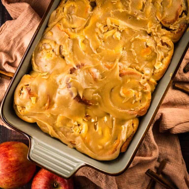 baking dish with apple cinnamon rolls topped with caramel frosting next to fresh apples.