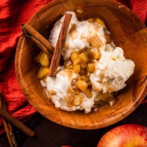 wooden bowl filled with ice cream and apple caramel topping and two cinnamon sticks