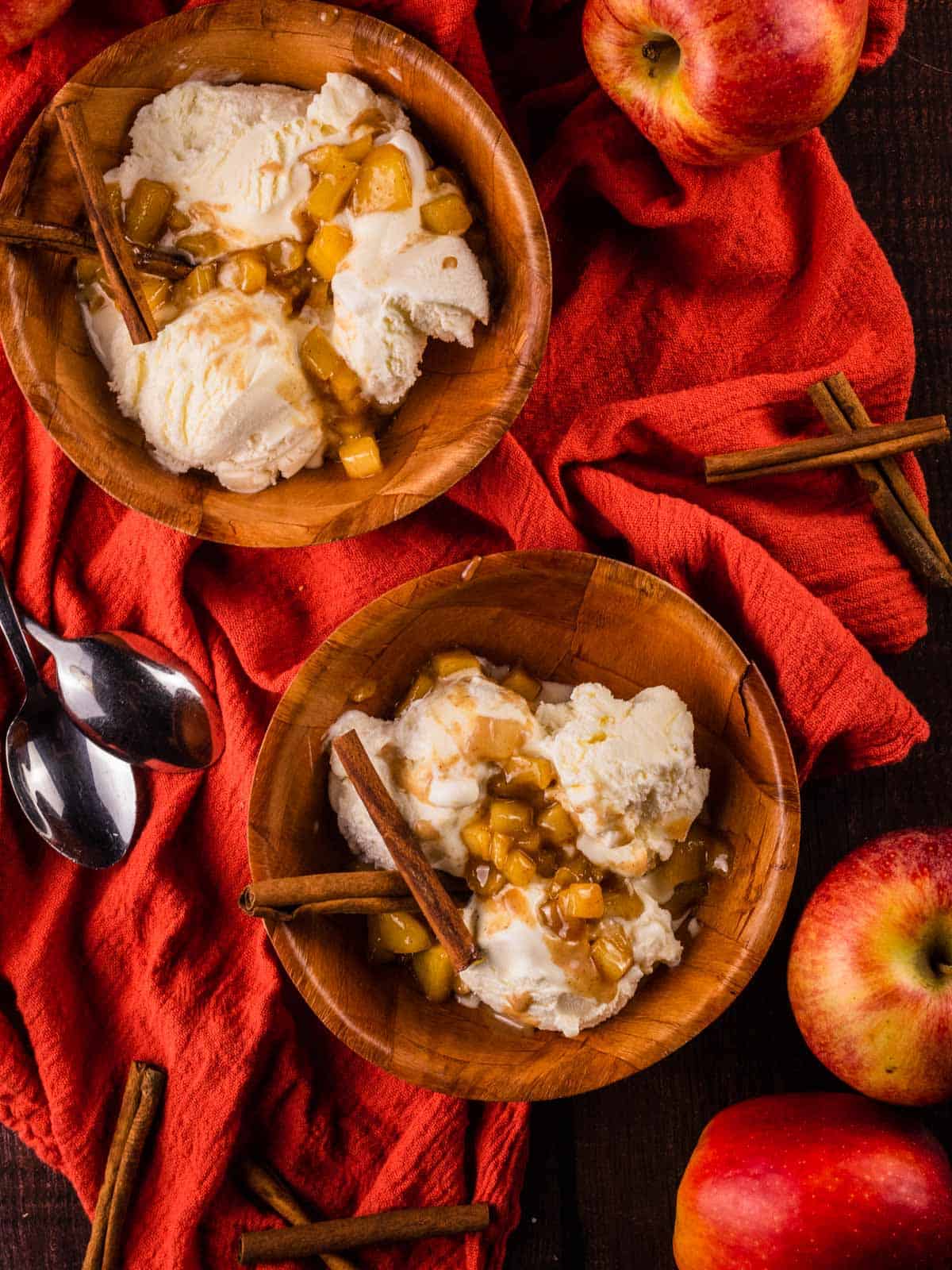 two wooden bowls filled with ice cream topped with caramel apple topping a cinnamon sticks