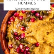 pumpkin hummus in a wooden bowl garnished with pomegranate seeds, pepitas and sesame seeds