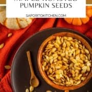 wooden bowl of roasted pumpkin seeds on a brown plate with pumpkins next to it
