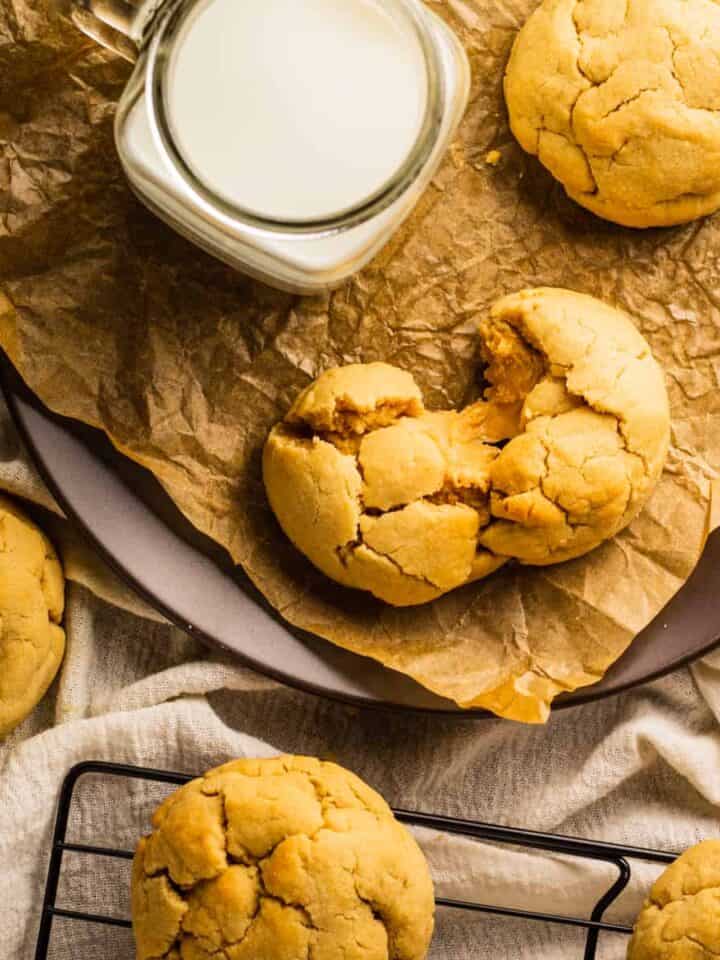 peanut butter cookies filled with peanut butter filling on a cooling rack and one broken in half on a plate next to a glass of milk