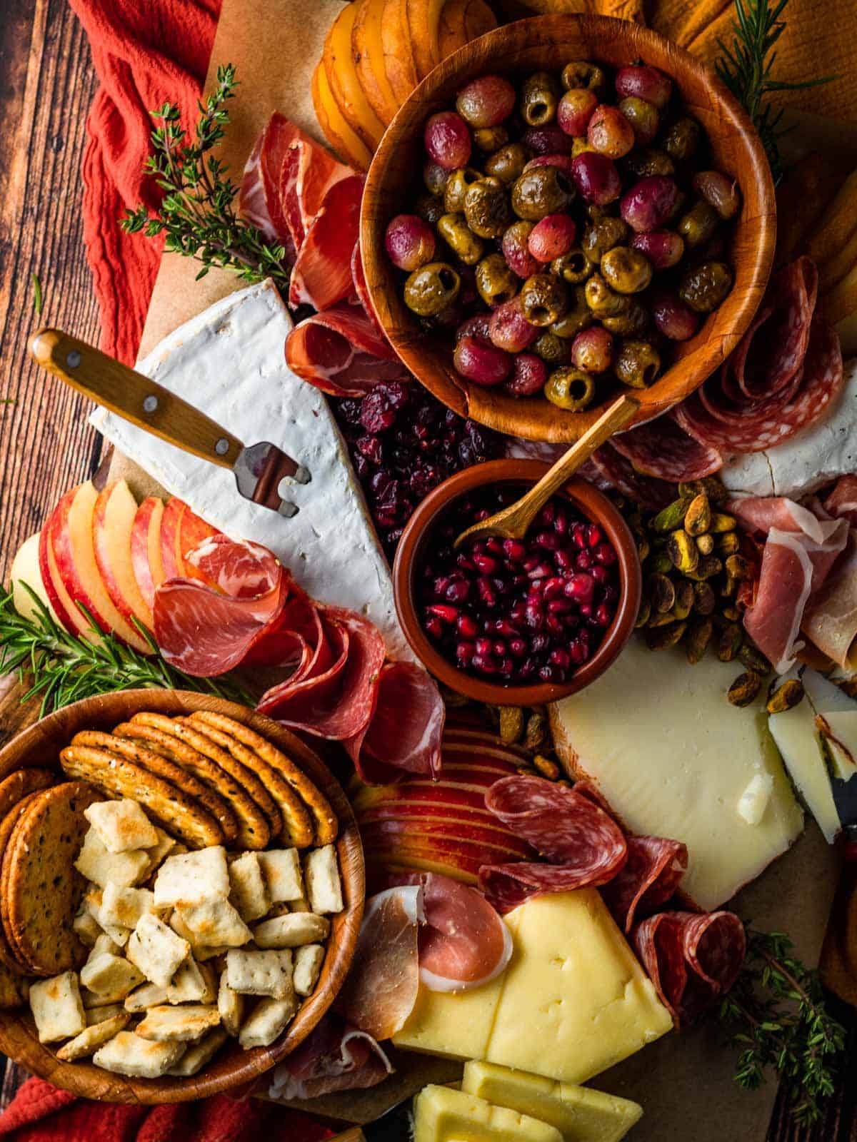cheeses, grapes and olives, crackers, pomegranate seeds and assorted cured meats, nuts and sliced fresh apple