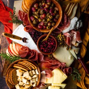 grapes and olives, cheese wedges, cured meats, crackers and fruits on a board.