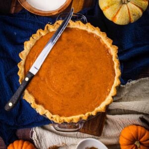 homemade baked pumpkin pie with a knife on it and fresh pumpkins around it