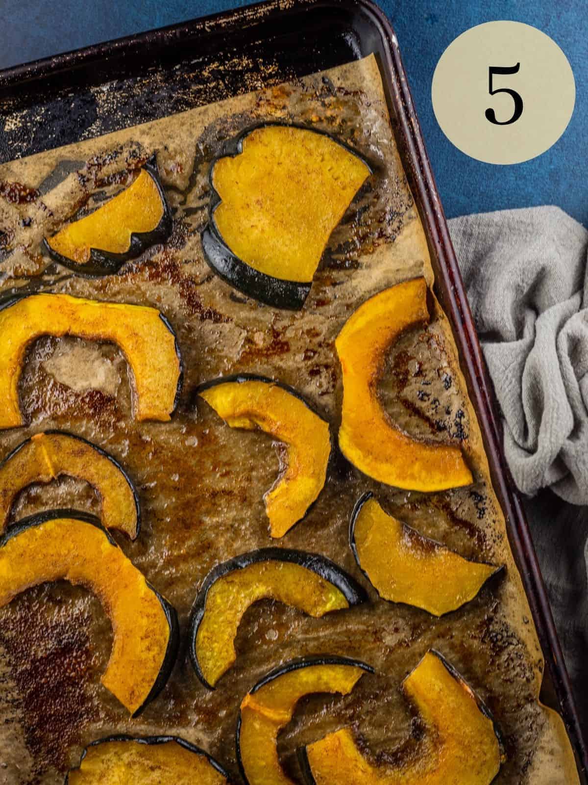 maple roasted acorn squash slices on a sheet pan on a gray towel on blue background