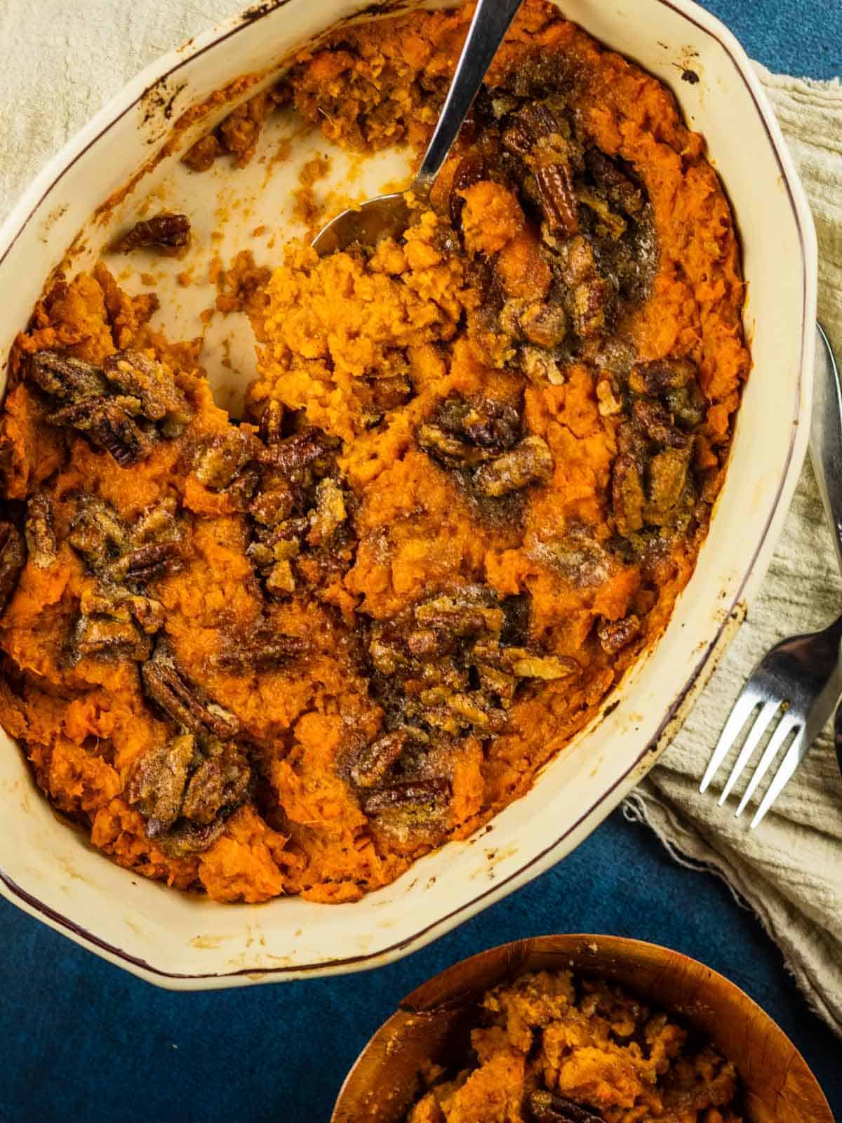 mashed sweet potatoes in a oval dish topped with pecan topping and a spoon scooping it
