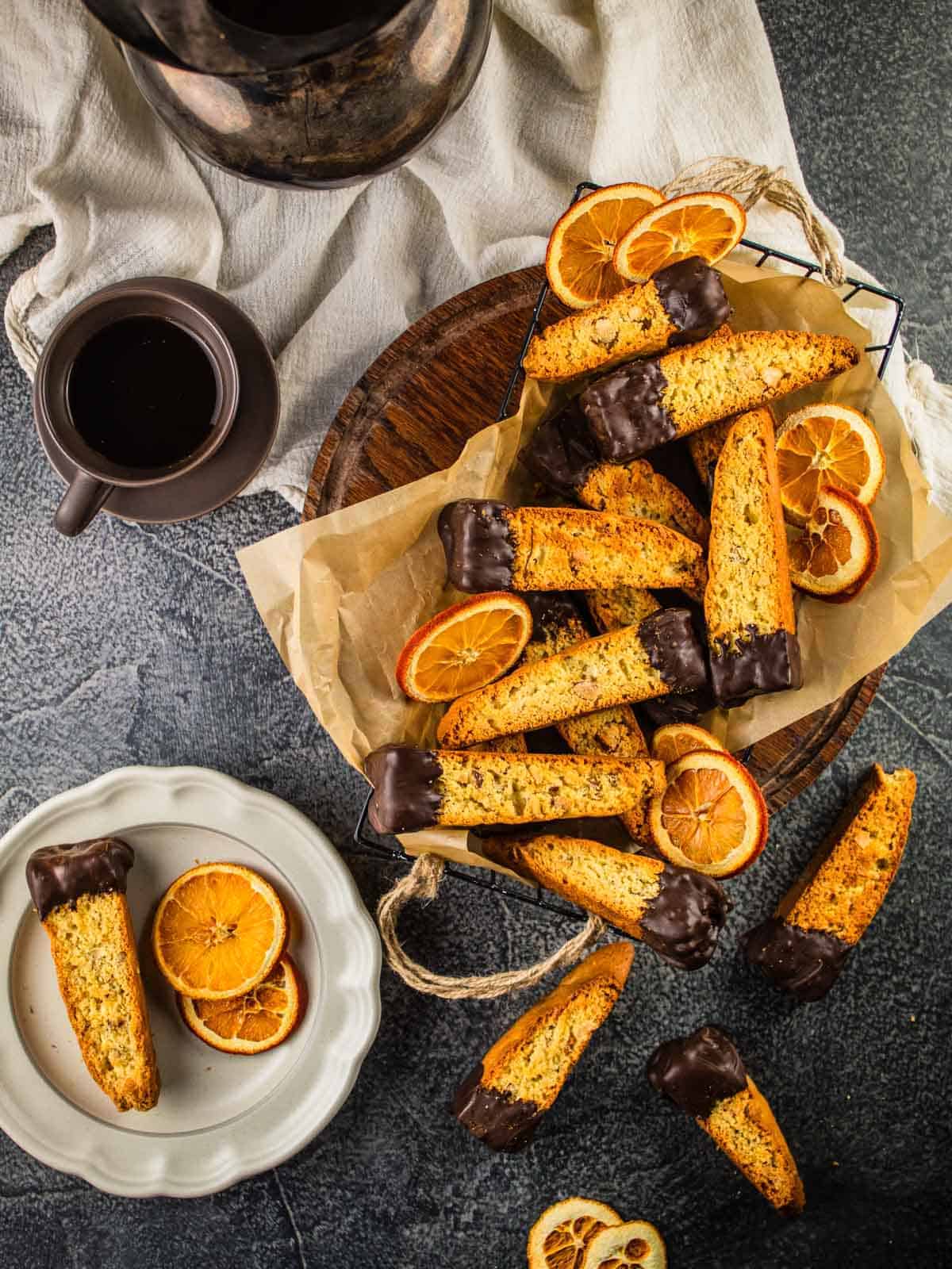 basket of biscotti with ends dipped in chocolate with dried orange slices and cup of coffee