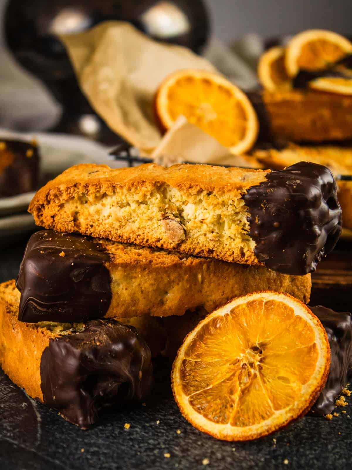 biscotti with ends dipped in chocolate stacked on each other next to dried orange slice