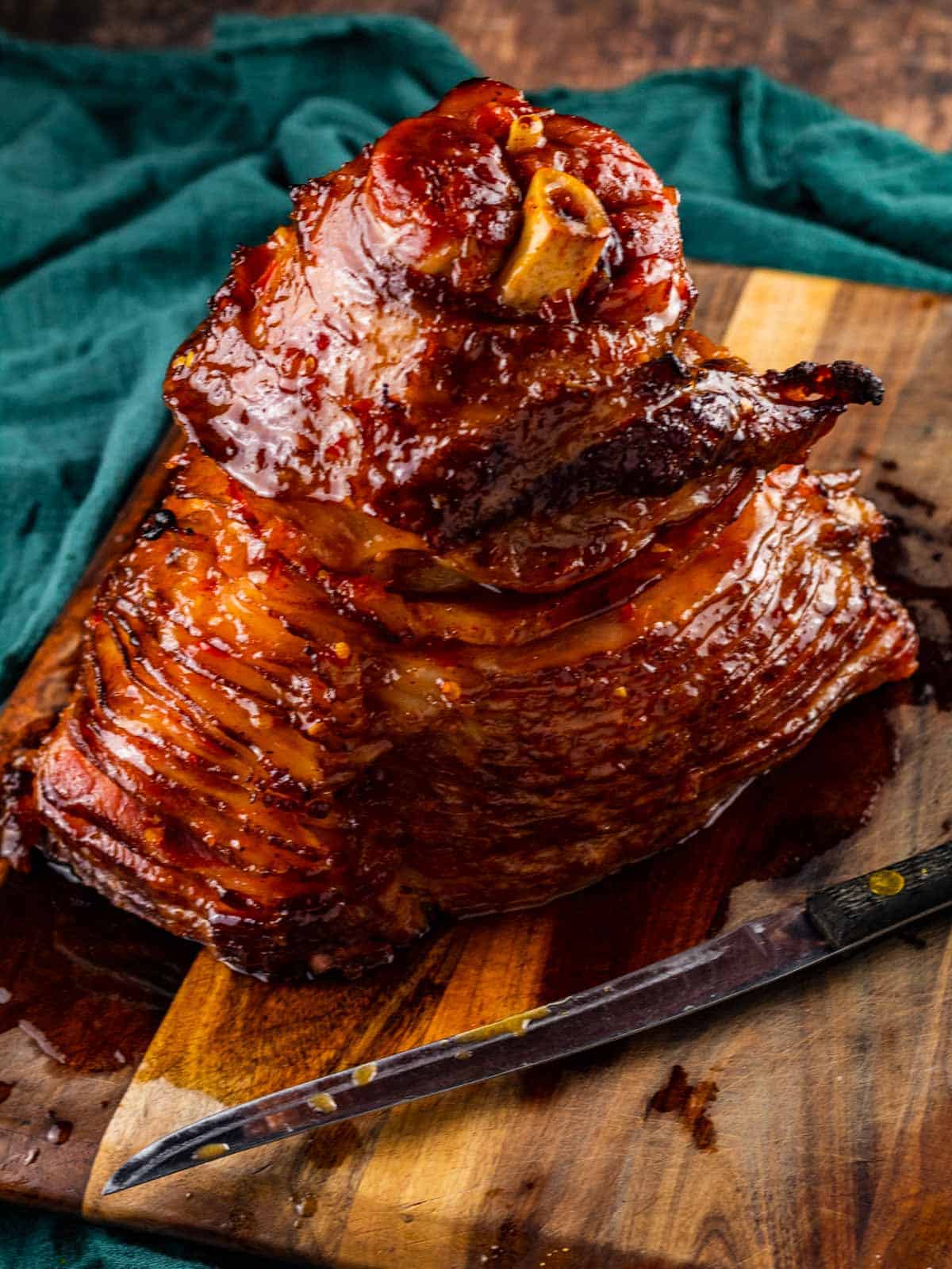 cooked spiral ham with glaze on a cutting board with a knife.