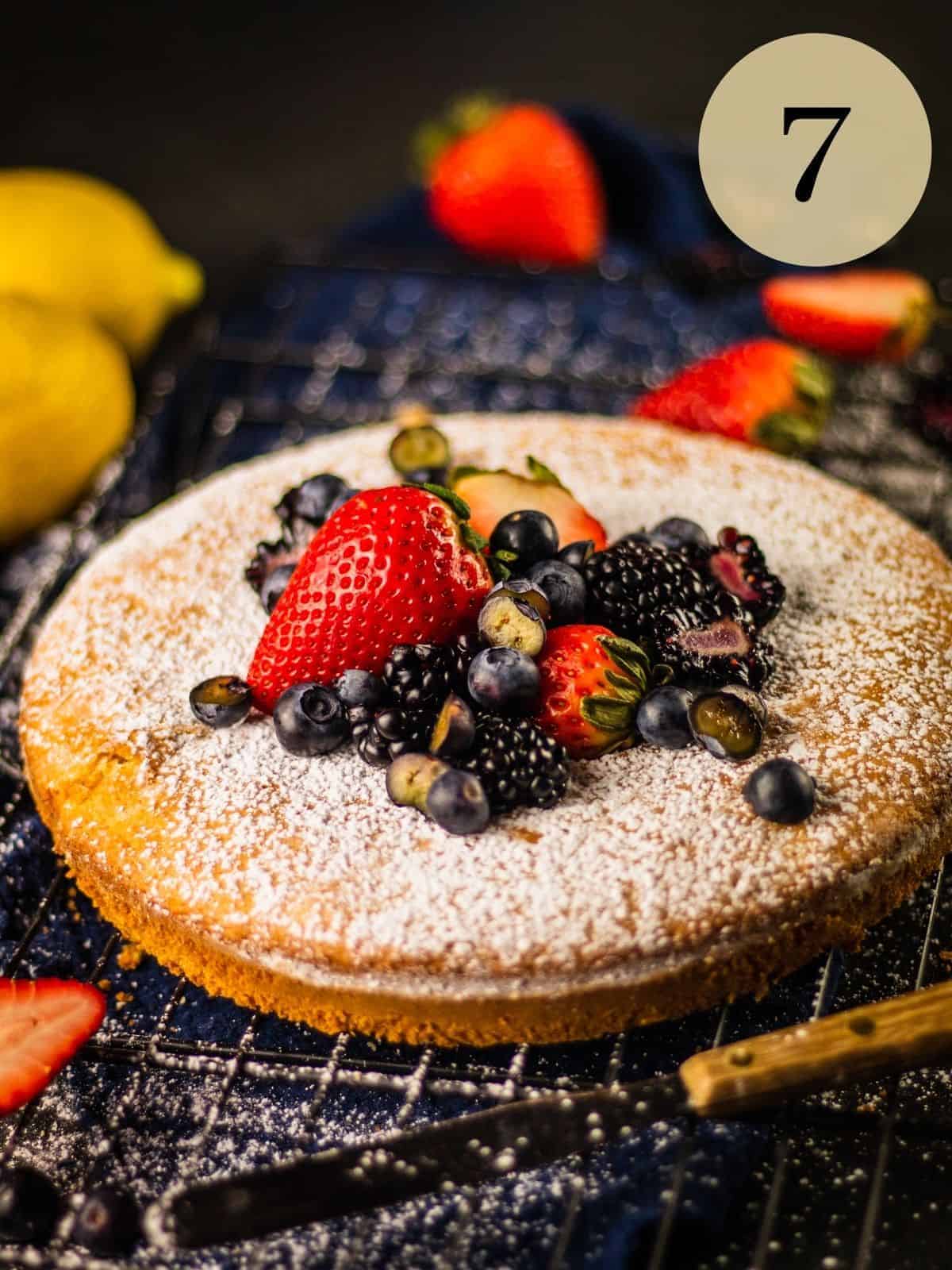 round olive oil cake on a cooling rack topped with powdered sugar and fresh berries