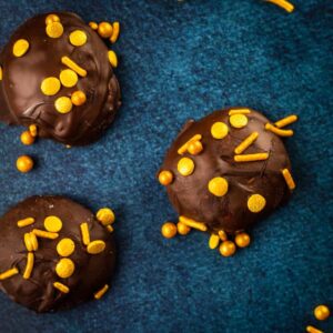 chocolate covered marshmallows with gold sprinkles on a blue table