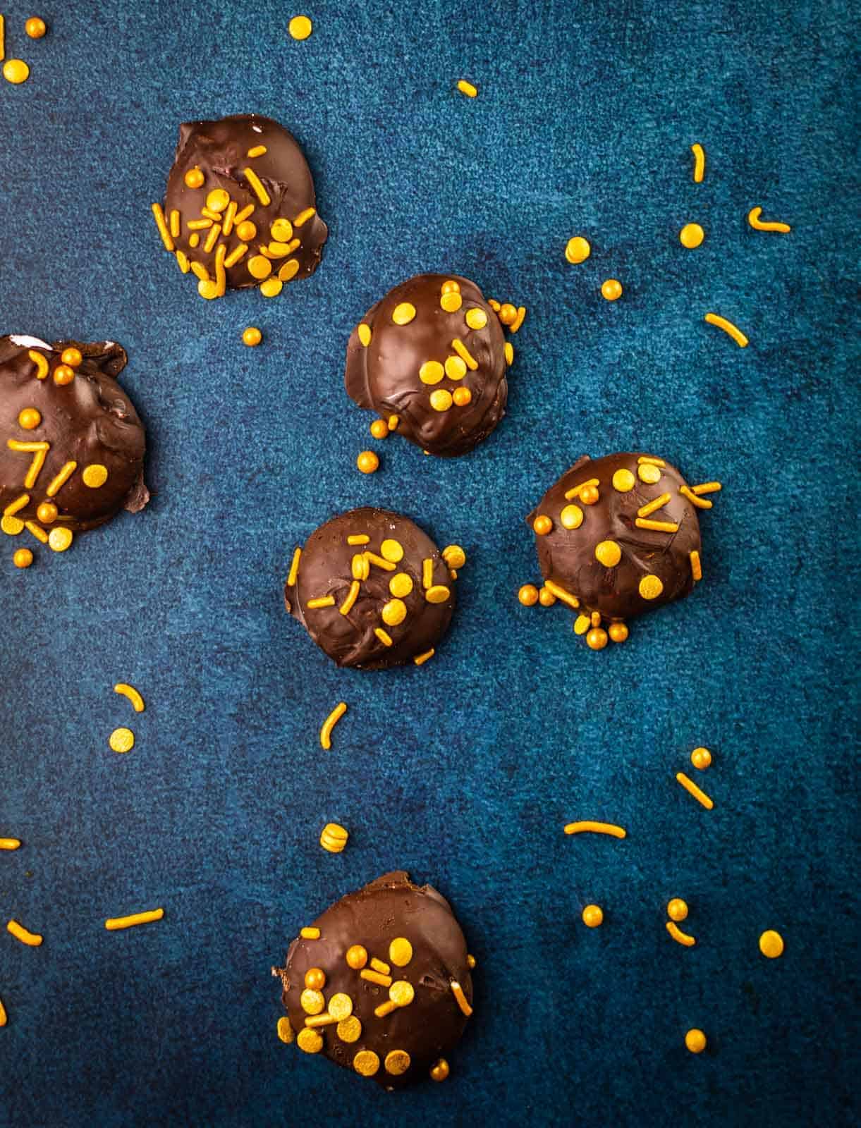round chocolate covered marshmallow candy with gold sprinkles on a blue table