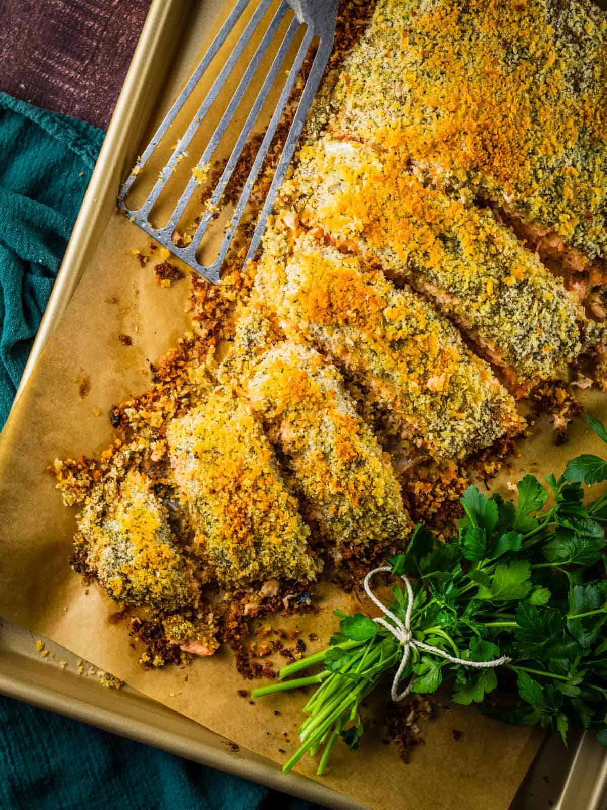 fiilet of panko crusted salmon partially sliced on a sheet pan with a metal spatula.