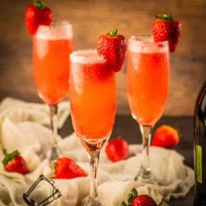 three champagne flutes filled with prosecco and strawberry puree and garnished with a fresh strawberry