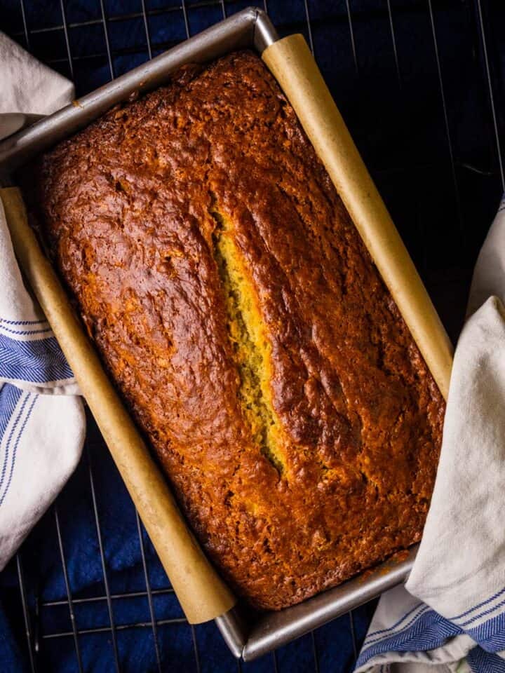 banana bread in a loaf pan with white and blue towels holding it