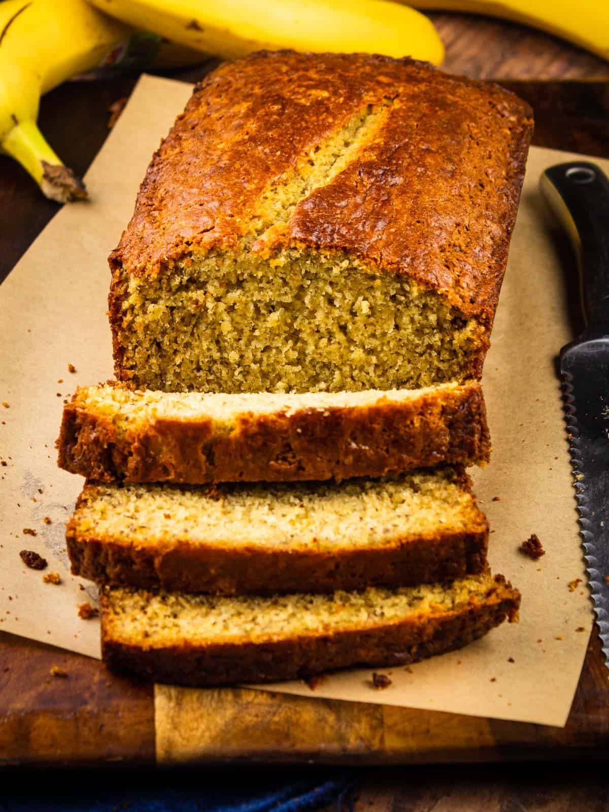 loaf of banana bread on a cutting board that is partially sliced with a knife