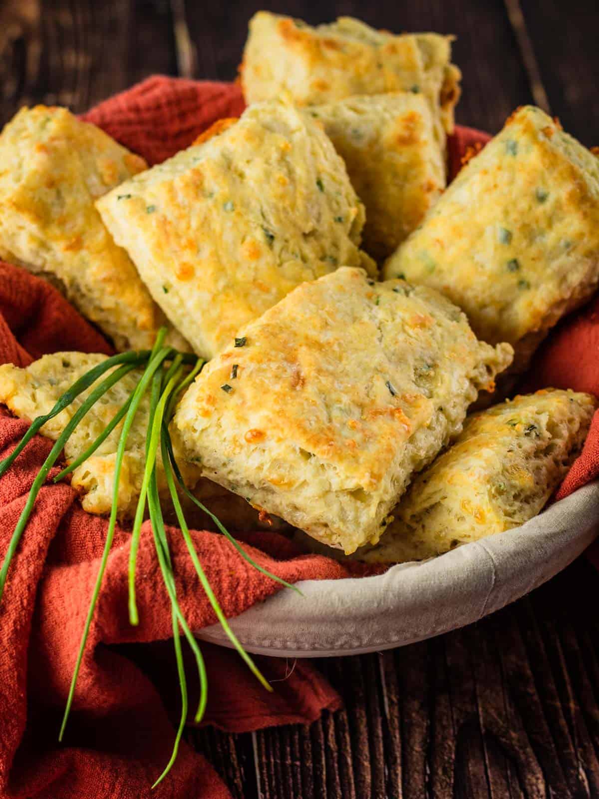 basket of rectangle shaped homemade cheddar chive biscuits with fresh chives next to it