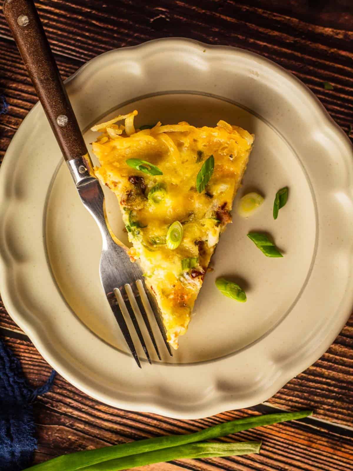 slice of quiche with hash brown crust on plate with fork garnished with sliced green onions