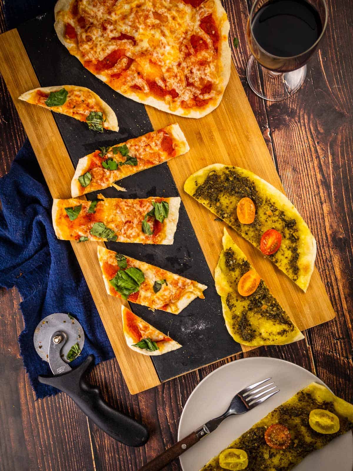 Sliced italian flatbread pizza on a wooden tray with a glass of wine next to it.