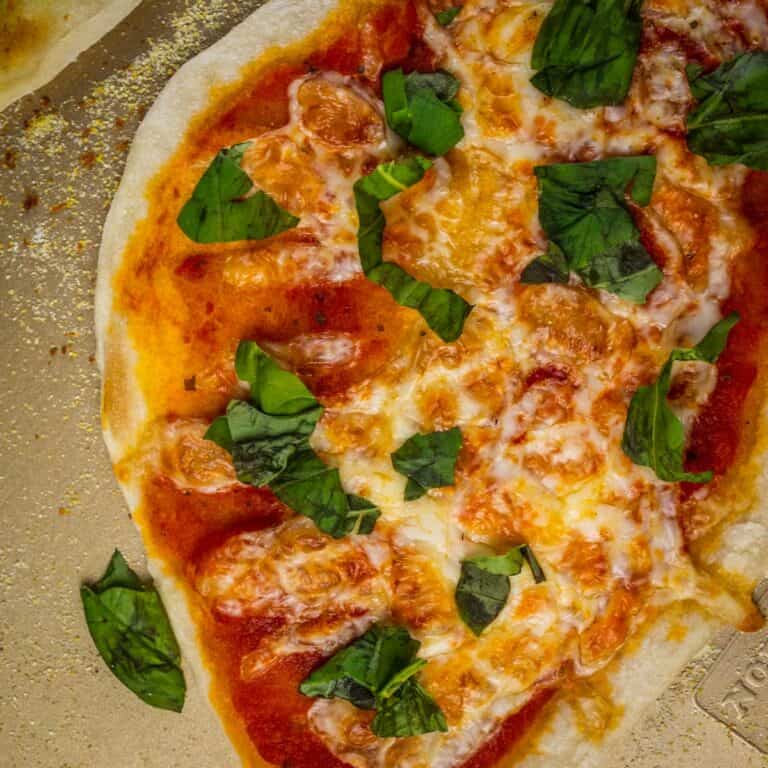 italian flatbread pizza topped with sauce, cheese and fresh basil on a sheet pan.