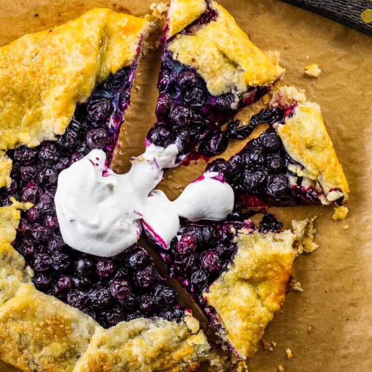 blueberry crostata with pieces cut from it topped with whipped cream on a sheet pan.