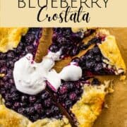 crostata with blueberries on a sheet pan with pieces cut from it and whipped cream.