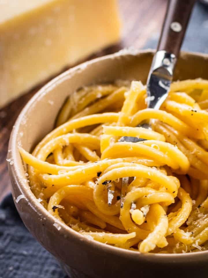 bucatini pasta topped with cheese and pepper swirled around a fork in a bowl.