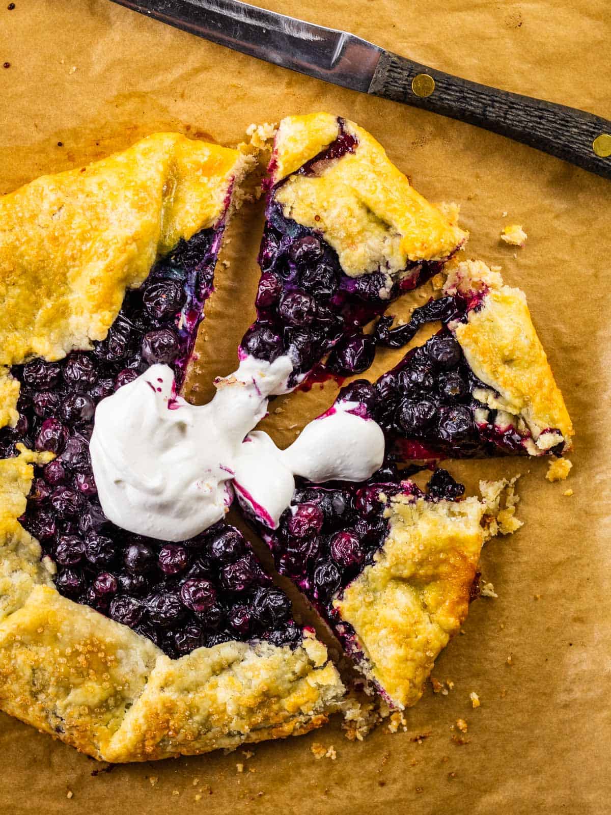blueberry crostata on a sheet pan topped with whipped cream with a few slices cut.