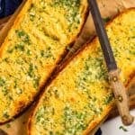 toast garlic herb and cheese bread on a sheet pan topped with a knife.