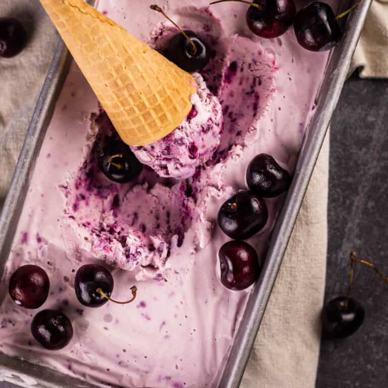 black cherry ice cream in a loaf pan with cone resting in it and fresh cherries around.