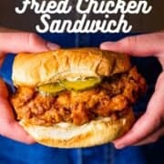 hands holding a fried chicken sandwich with pickles and mayo.