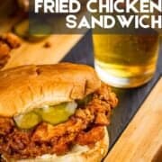 buttermilk fried chicken sandwich with mayo and pickles on a wooden tray with beer behind.