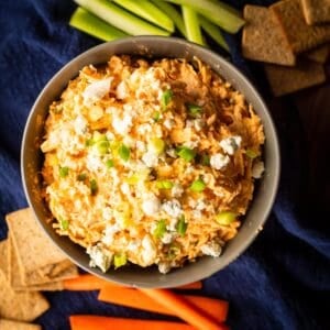 buffalo chicken dip in a bowl topped with blue cheese and green onions.