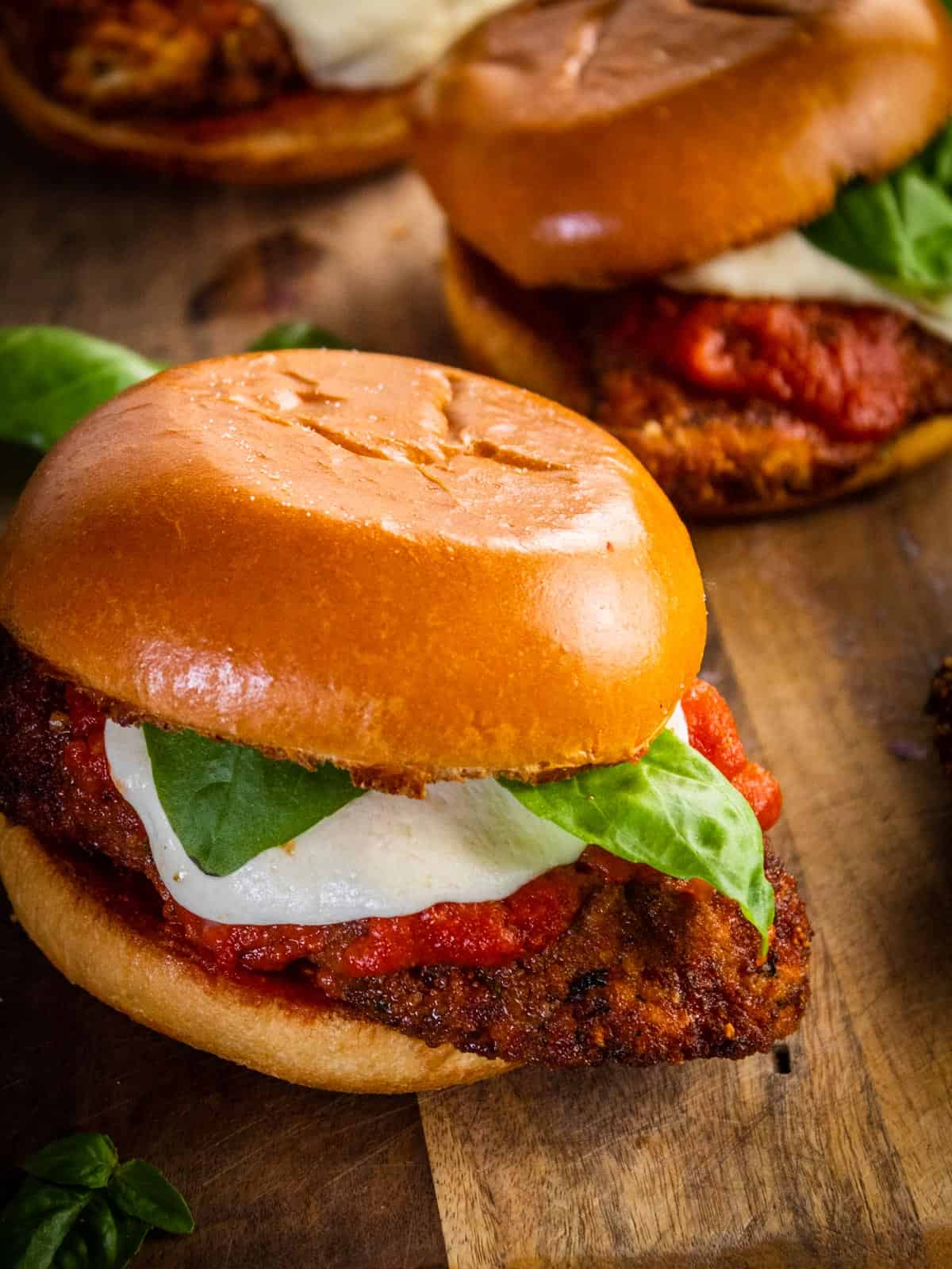 chicken parm sandwich topped with mozzarella, sauce and fresh basil on a cutting board.