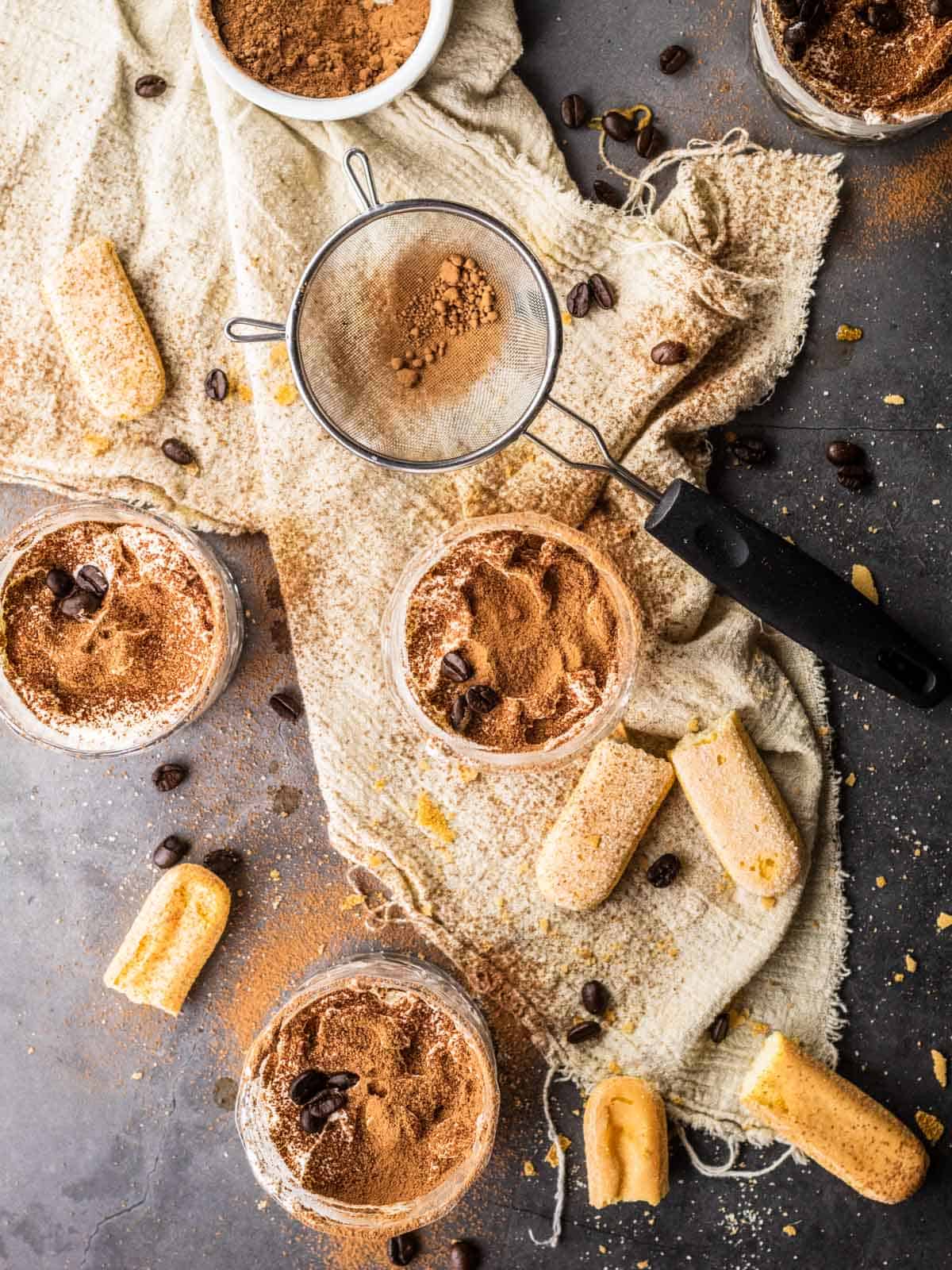 glasses filled with tiramisu dusted with cocoa powder and topped with whole coffee beans.