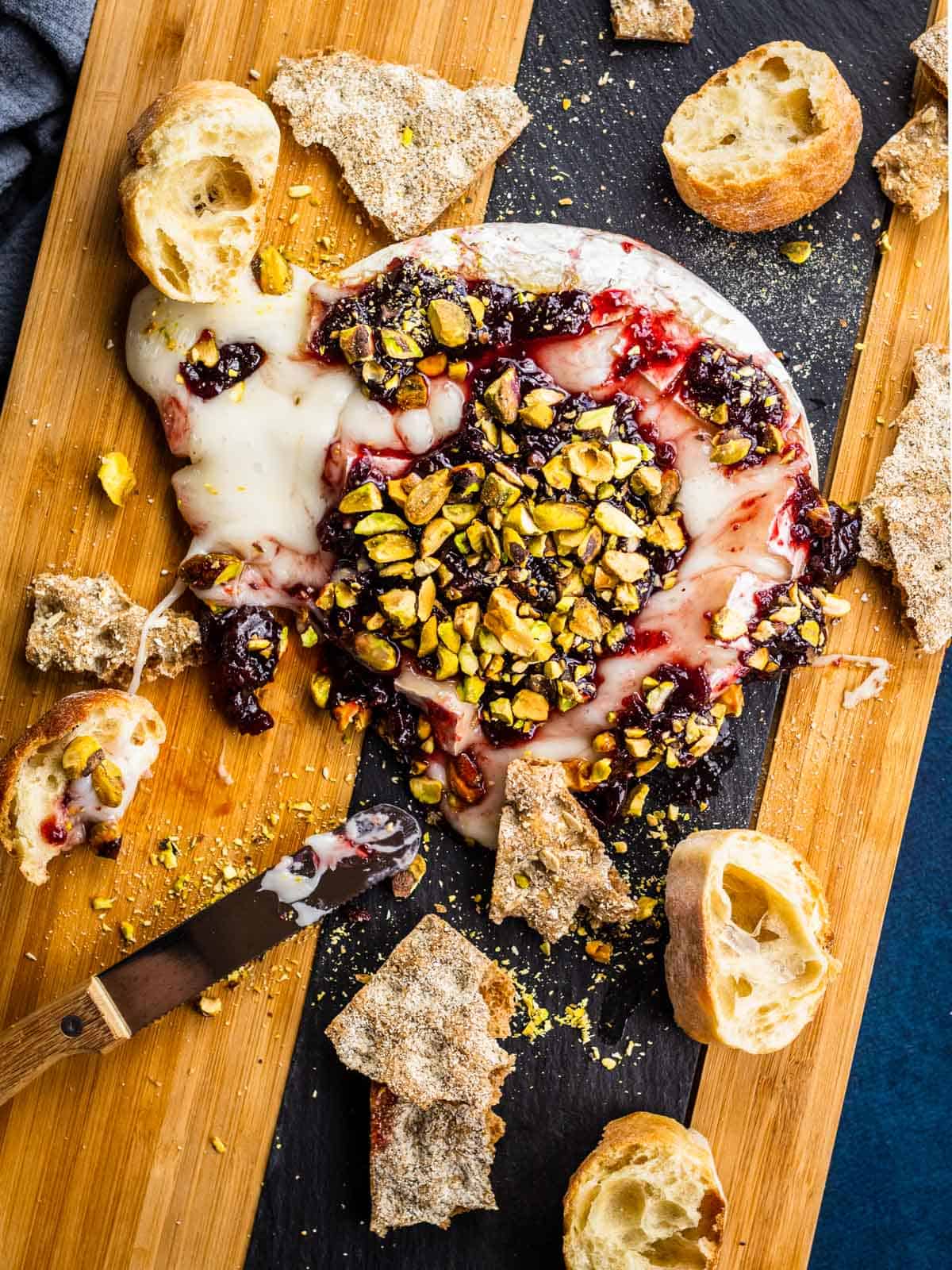 partially melted wheel of brie on cutting board with jam and nuts and bread around.