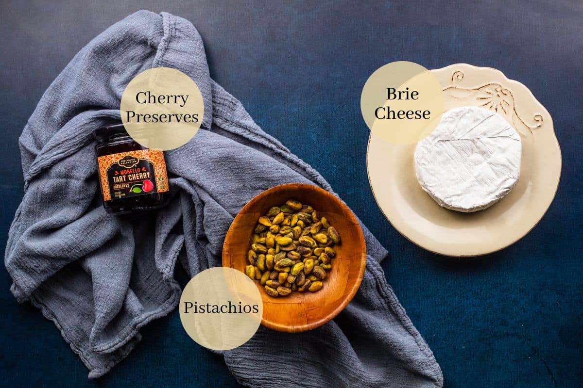 wheel of brie cheese, jar of sour cherry preserves and bowl of roasted shelled pistachios.